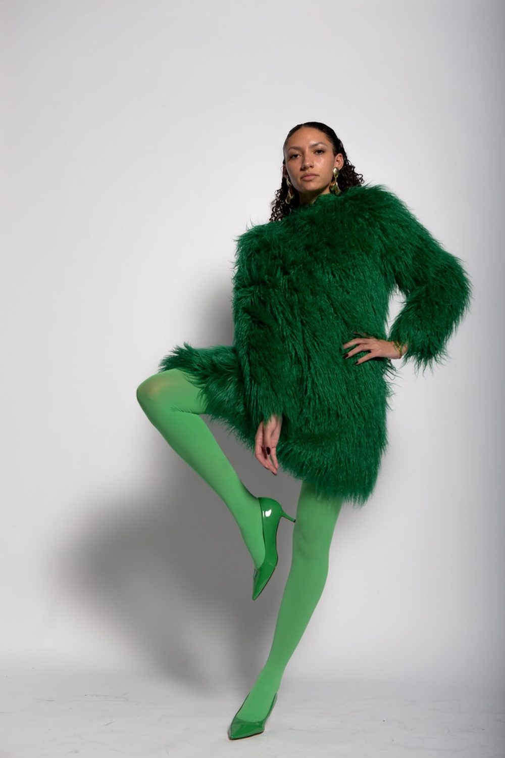 The glamour look standing — the emerald shaggy coat worn as a dress over bright green tights and green heels