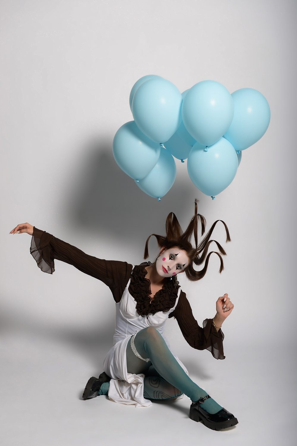 The King Kong styling — kneeling on a studio floor with one arm thrown out, knotted horned hair, theatrical clown make-up and a bunch of pale blue balloons
