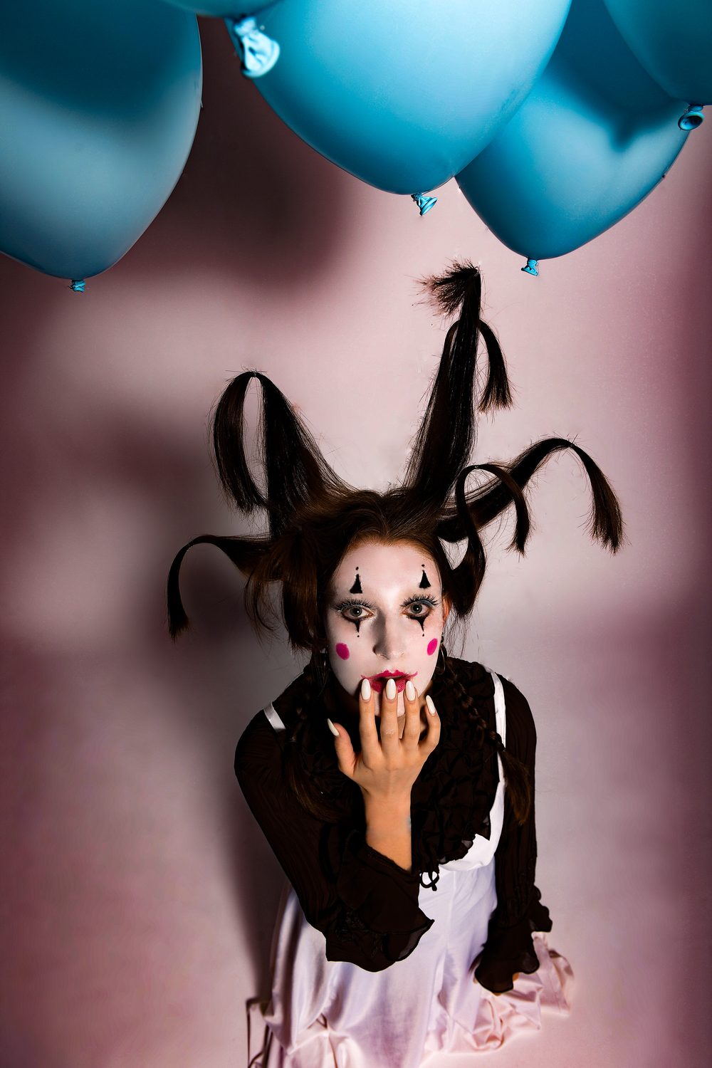 The King Kong styling against a pink ground with pale blue balloons overhead, knotted horned hair and theatrical make-up