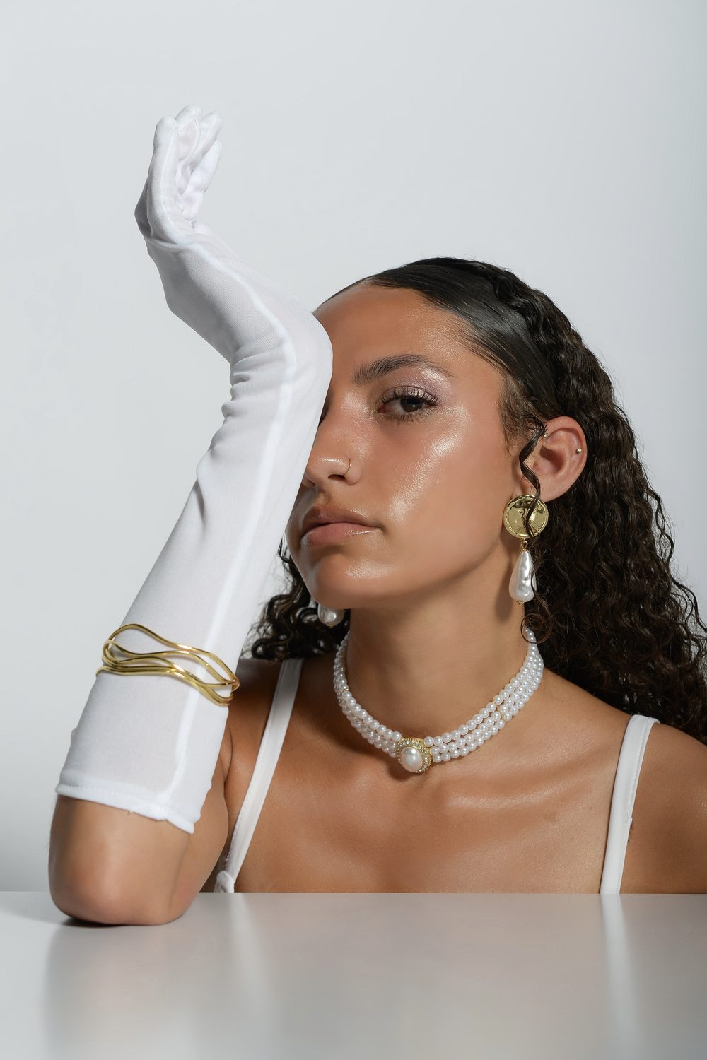 The Harper’s Bazaar styling with one gloved arm raised across the face, a gold cuff at the wrist and a pearl choker