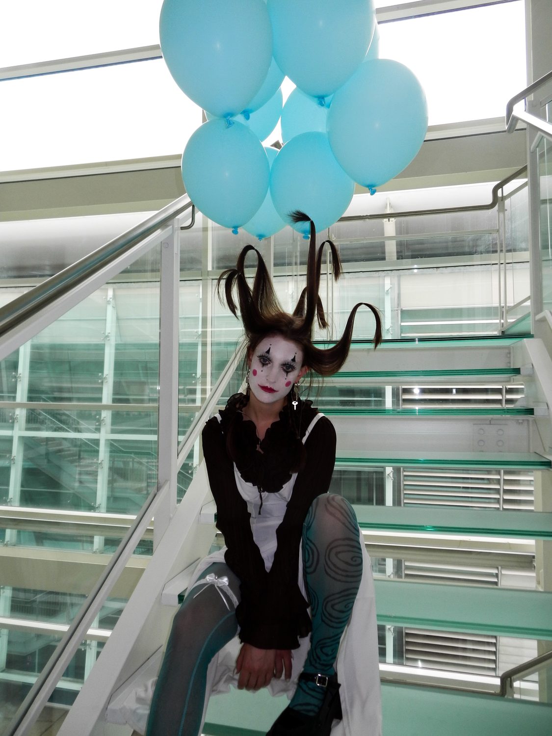 The King Kong styling crouched on a teal municipal staircase behind glass, balloons above, dark layers over tights