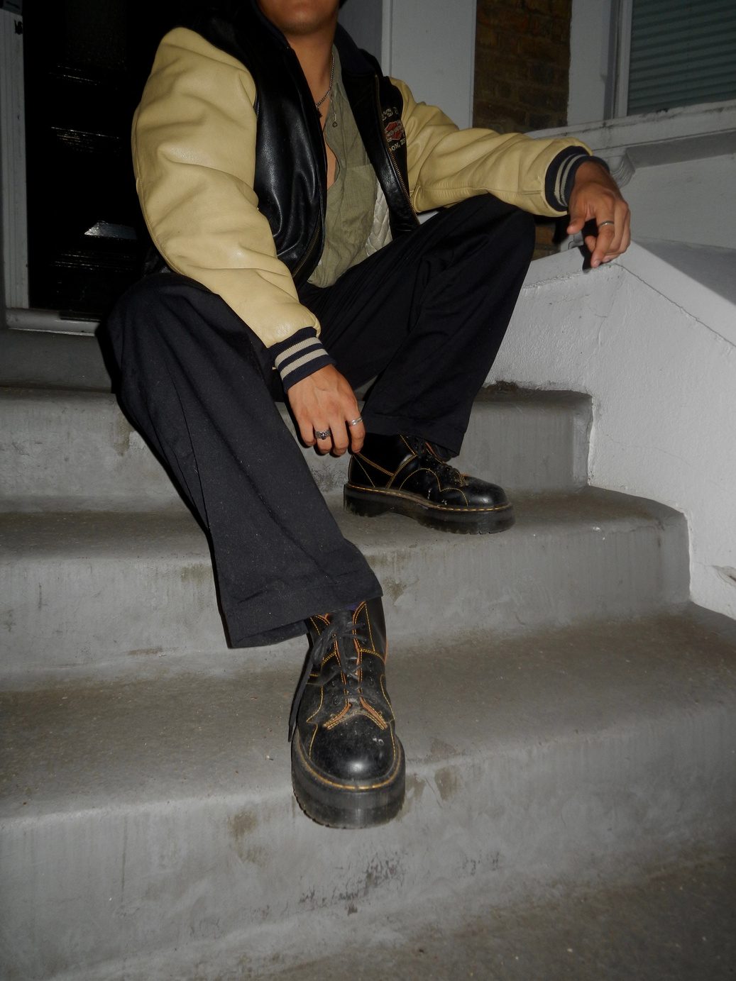 Participant 002 seated on stone steps with legs crossed, cream V-neck jumper, black wide-leg trousers and Doc Martens