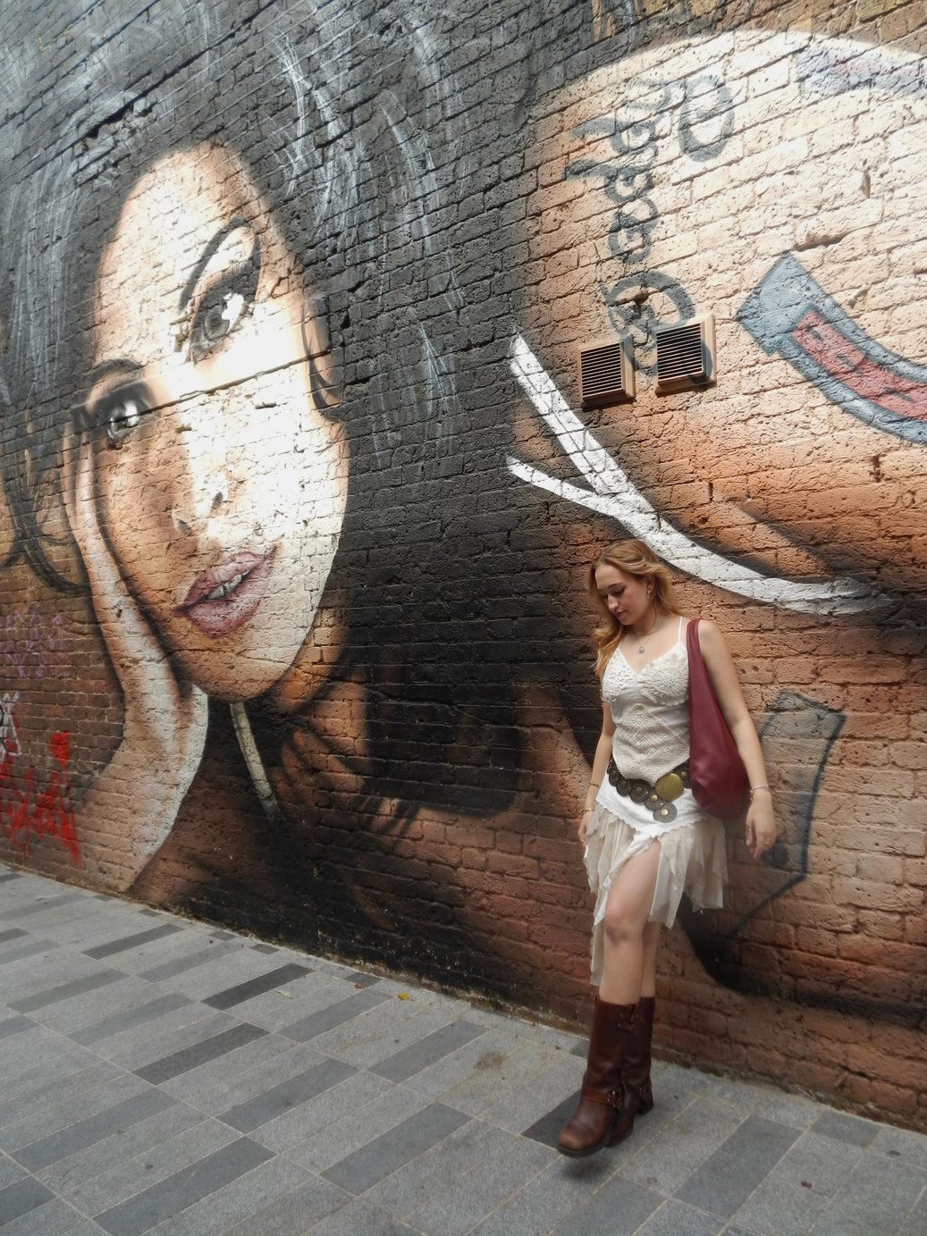 Participant 003 against a large painted wall mural, white lace dress, concho belt and brown cowboy boots