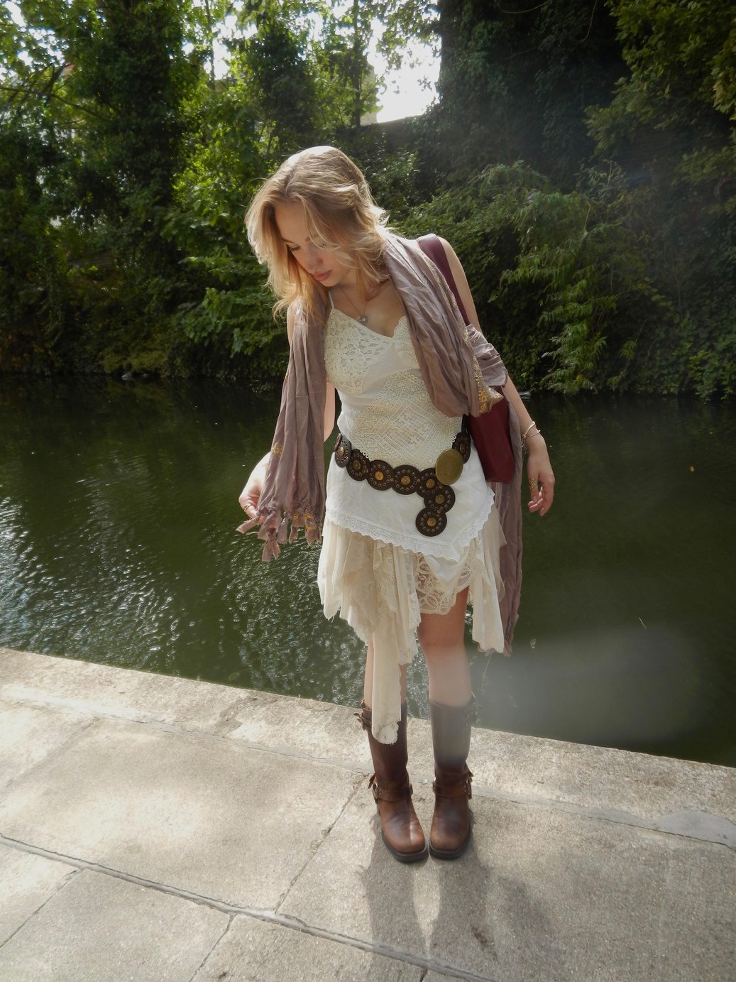Participant 003 standing full length beside water at dusk, white lace dress with a draped wrap over one shoulder, concho belt and cowboy boots