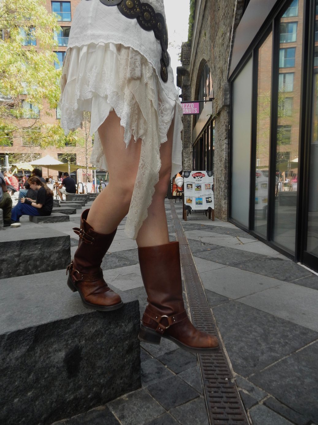 Cropped street frame of participant 003 — brown cowboy boots and the hem of the white lace dress on a stone step, shopfronts behind