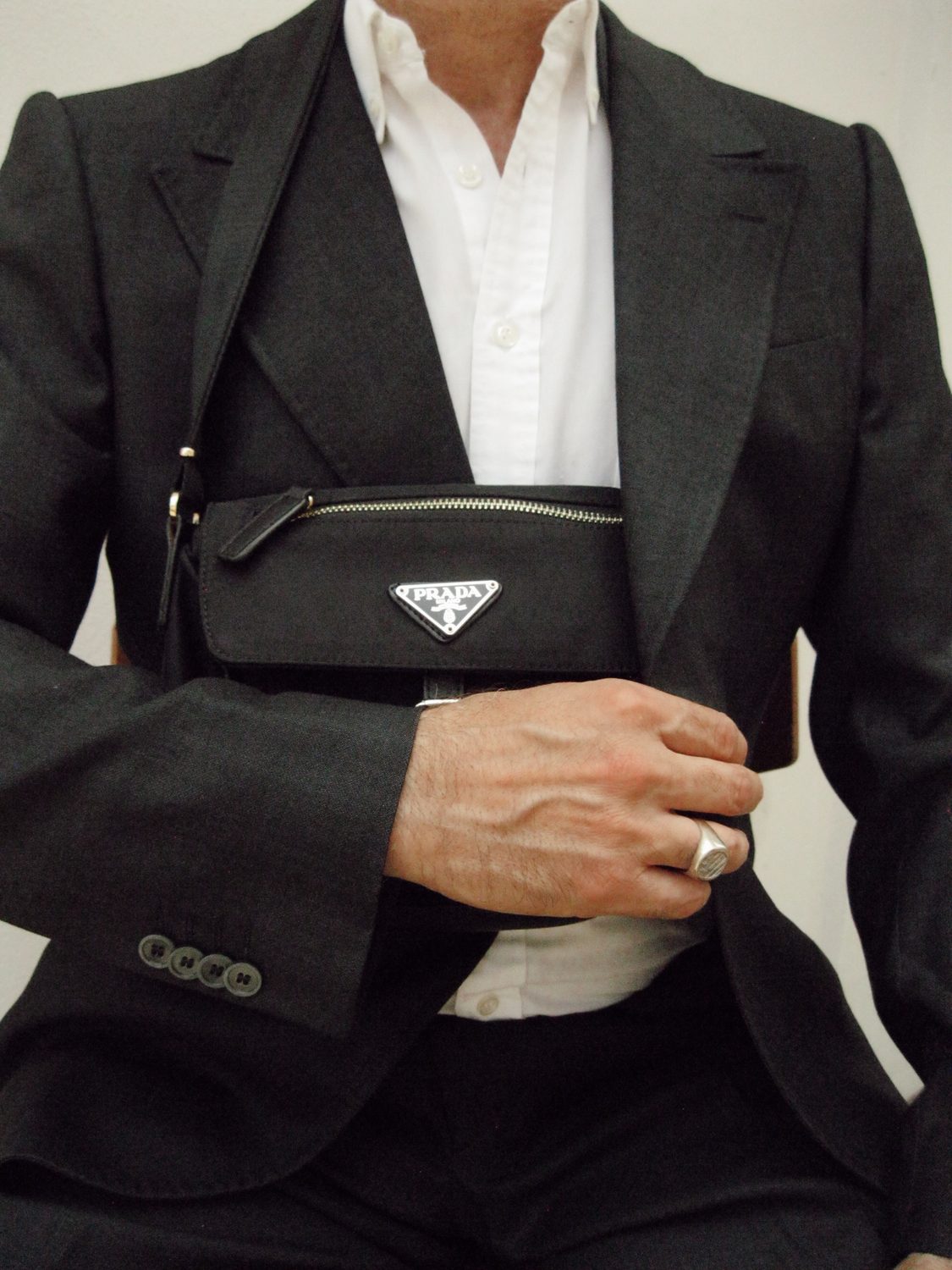 Torso crop of charcoal tailoring over a white shirt with a black crossbody strap across the chest