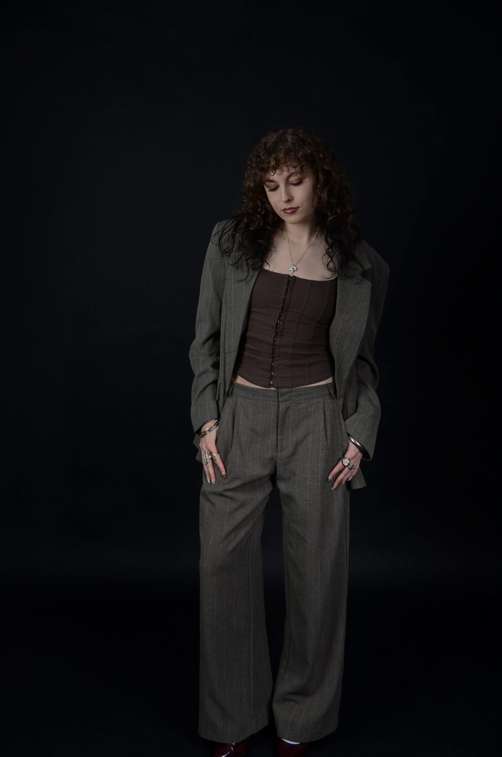 The feminine reading on a black backdrop — the blazer worn open over the corset top and wide-leg trousers, hands loose at the sides