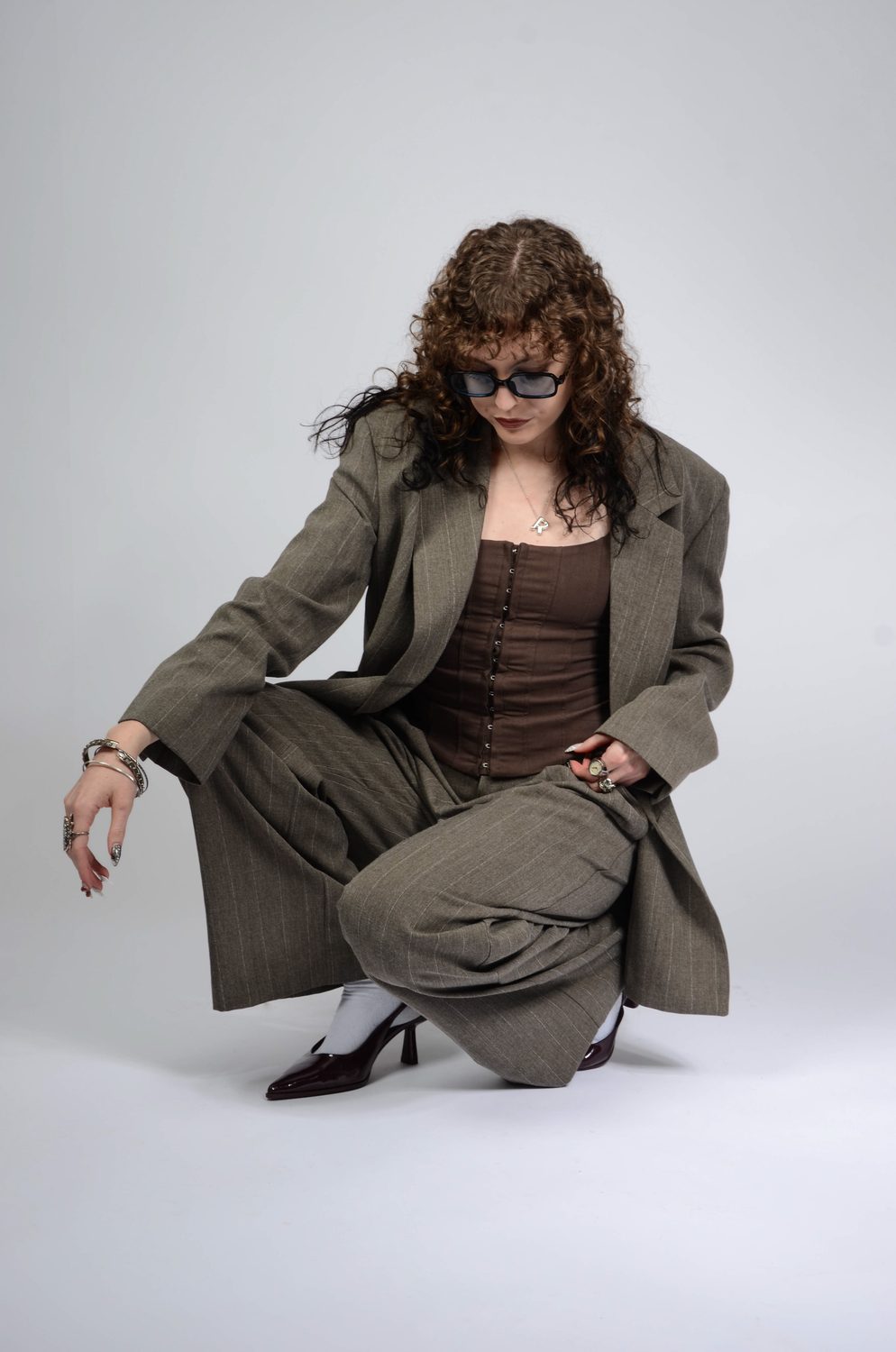 Crouched low on a pale backdrop, one arm extended along the knee, the oversized blazer pooling onto the floor