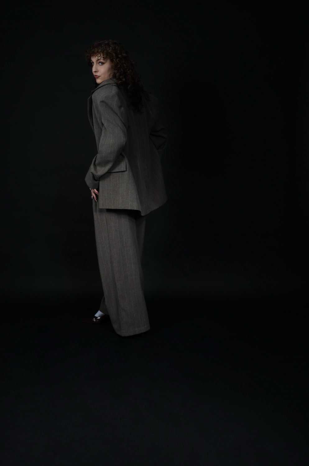 Turned away from camera on a black backdrop, the jacket seen across the shoulders, hair falling over the collar