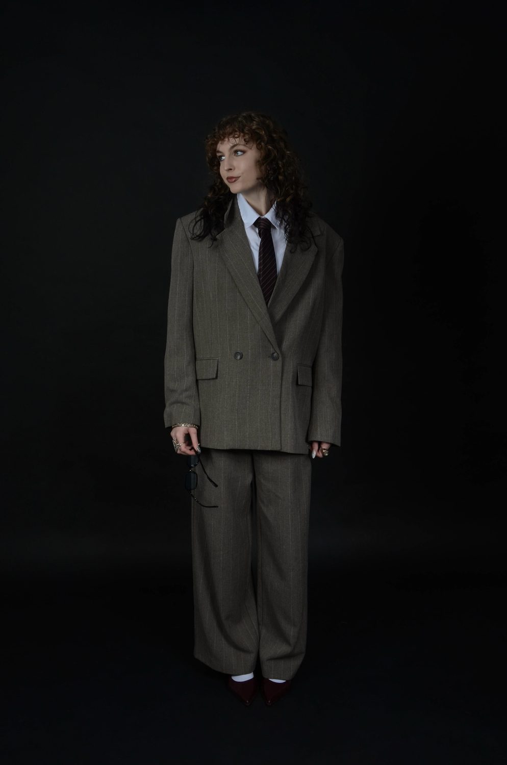 The masculine reading full length on black — shirt and tie, arms squared at the sides, chin lowered